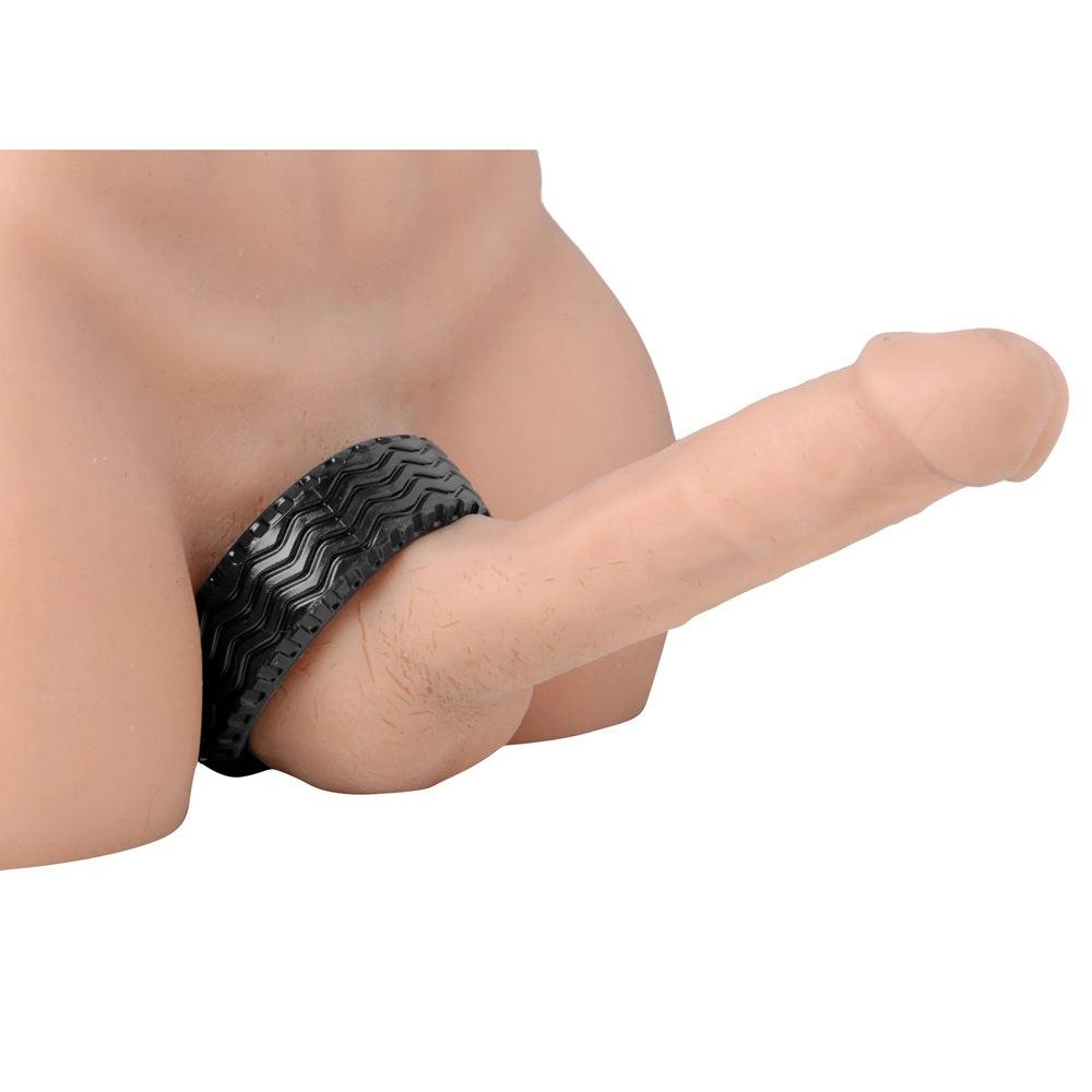 Black tire-style cock ring worn around both the cock and balls on a prosthetic penis on a white background