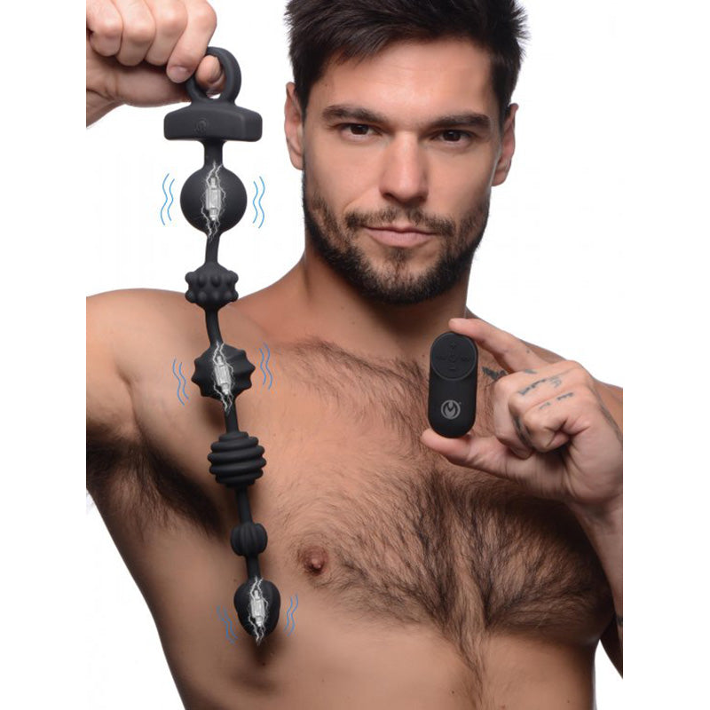Man holding finger loop of 21X Dark Rattler Vibrating Silicone Anal Beads and remote control, showing vibrating motors in three of the six beads
