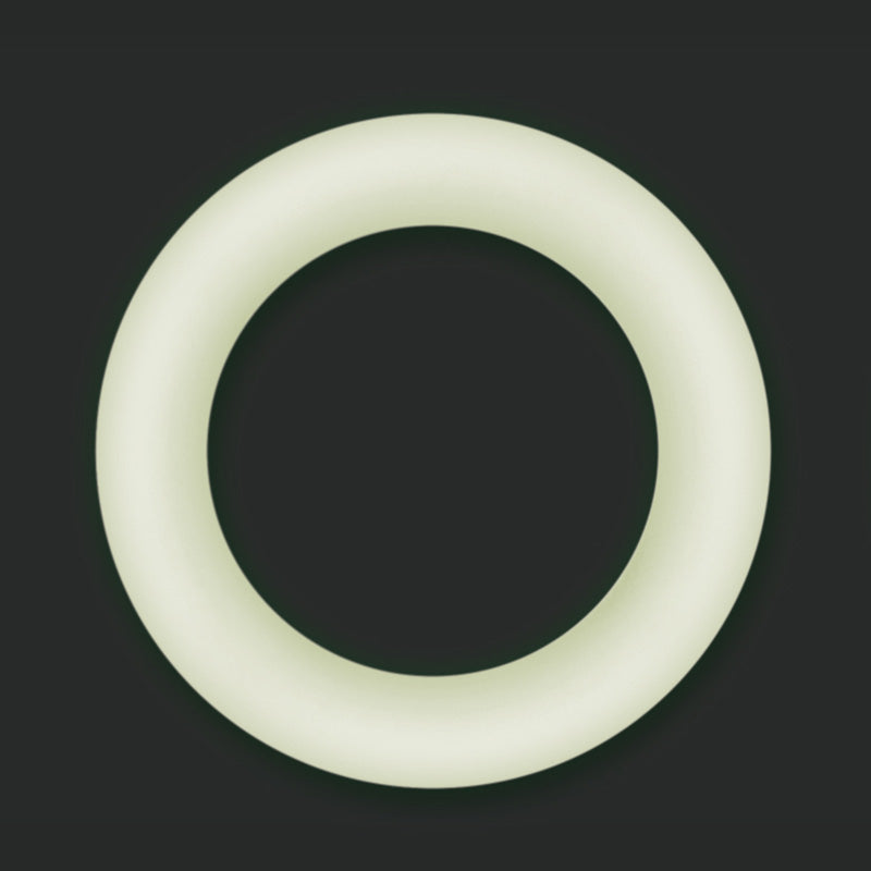 Small clear Firefly Halo glow-in-the-dark cock ring glowing on a dark background